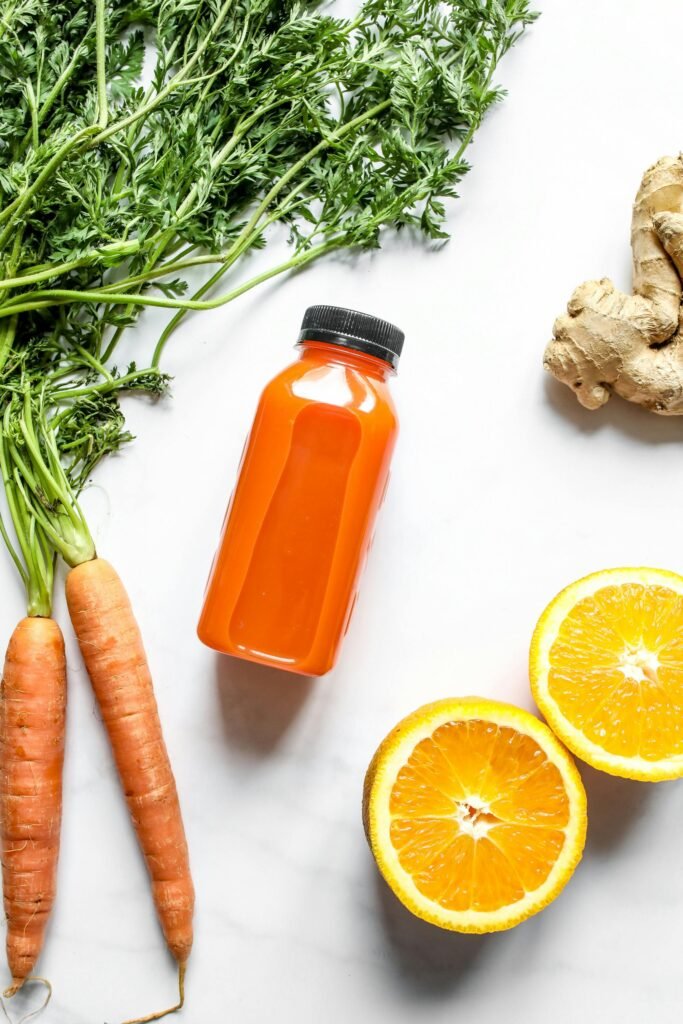 Vibrant orange juice bottle surrounded by fresh carrots, orange slices, and ginger.